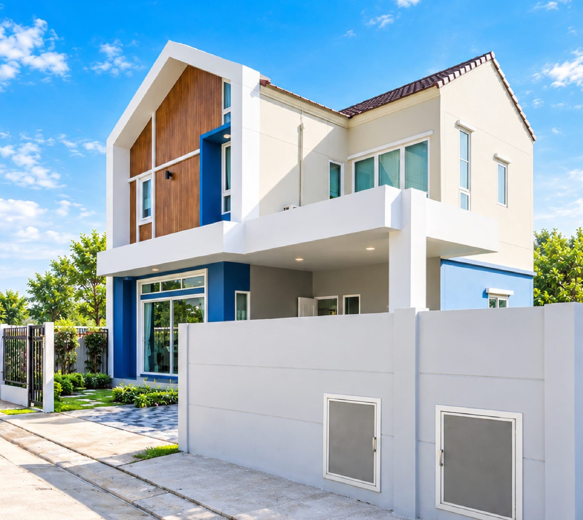 The two-storey house, with a timber-clad gable and white and blue walls behind a white boundary wall.