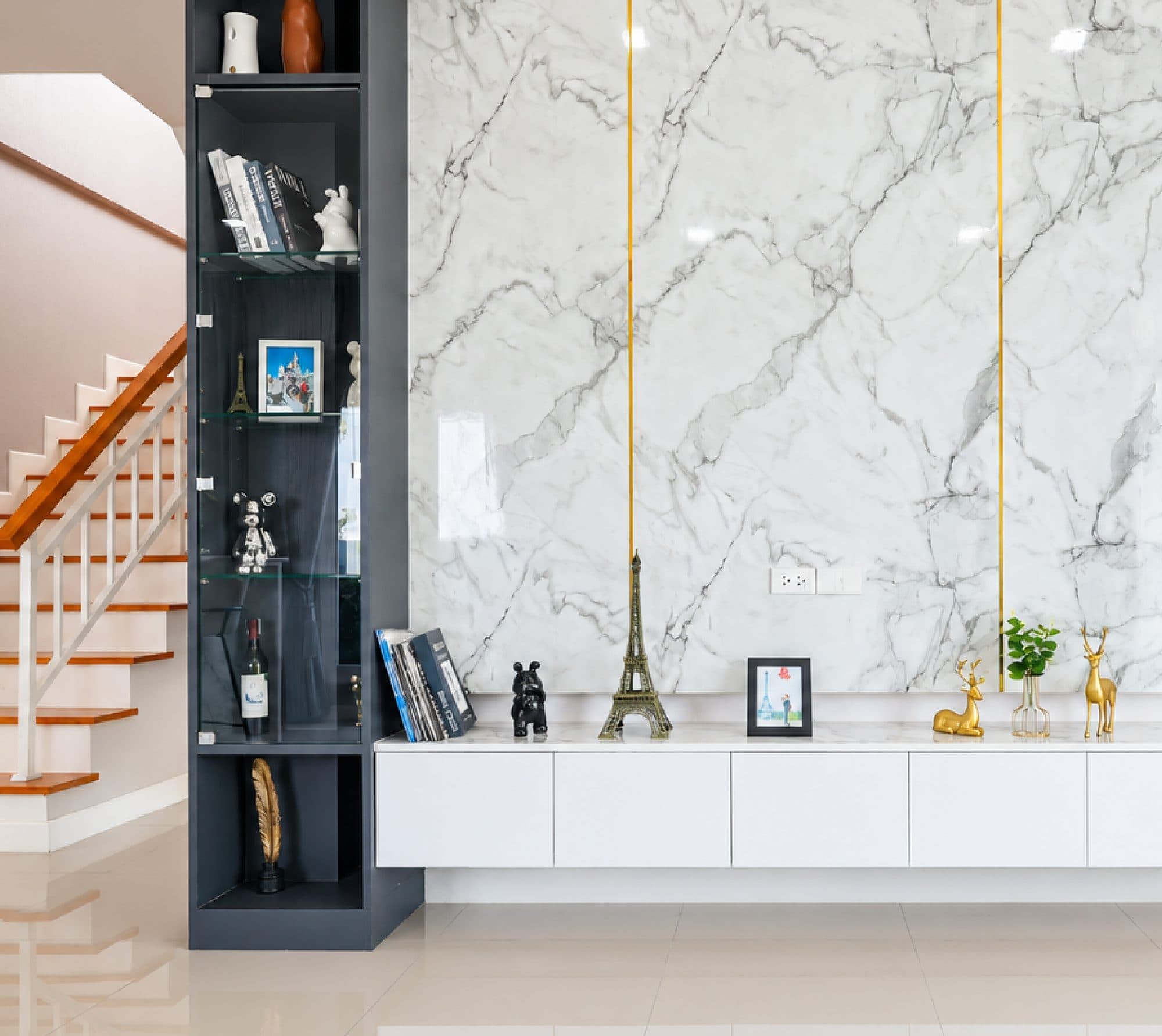 Marble TV wall with gold inlay, beside a display shelf and the stair.